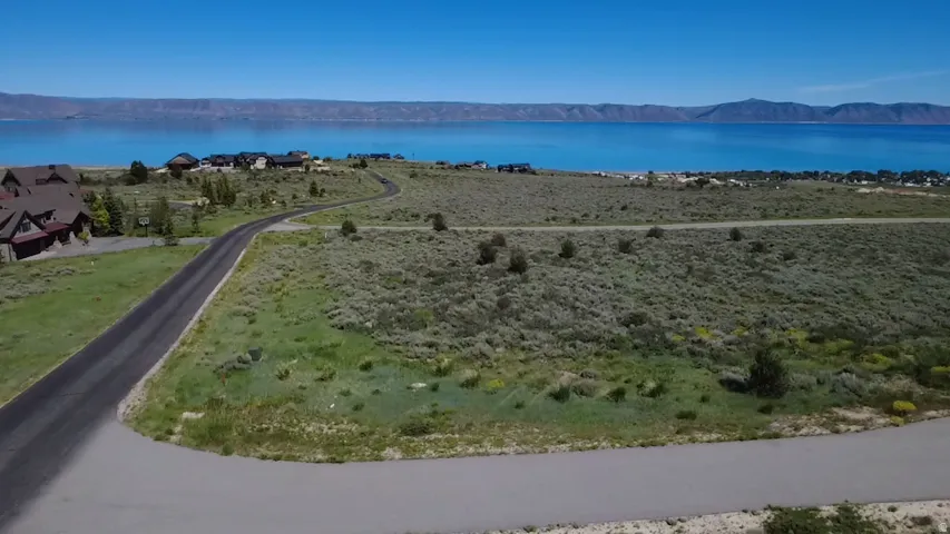 Expansive land parcel featuring natural shrubbery and a paved road, situated with a lake and distant mountains forming a natural backdrop