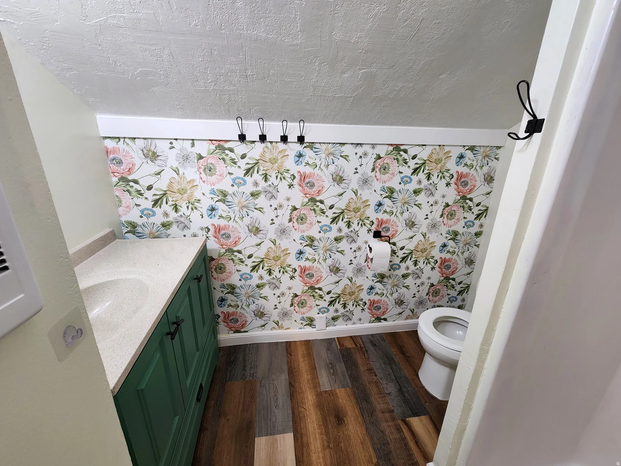 Bathroom with vanity, dark wood finished floors, a textured ceiling, and wallpapered walls