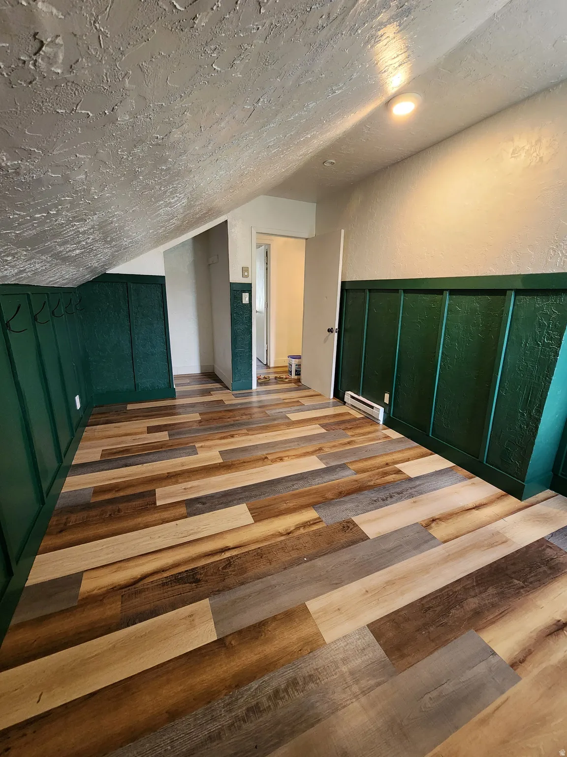 Bedroom with wood finished floors, a textured wall, a baseboard heating unit, and a decorative wall