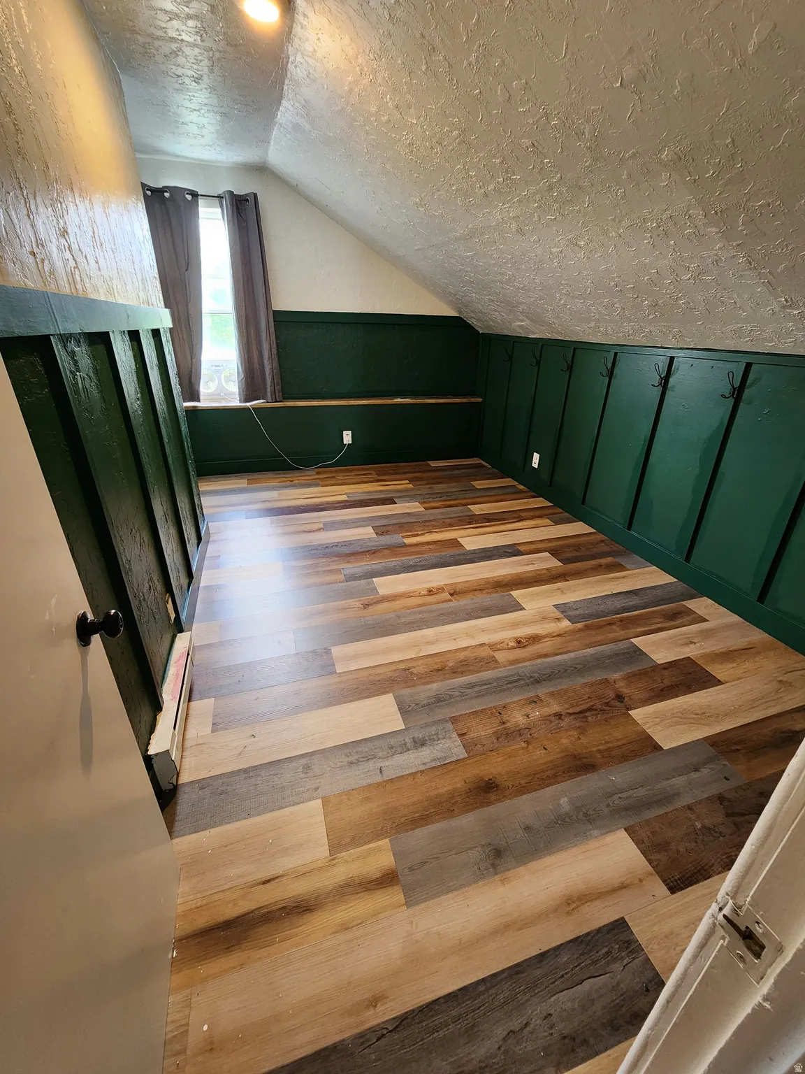 Bedroom with light wood-type flooring, lofted ceiling, a wainscoted wall, and a decorative wall