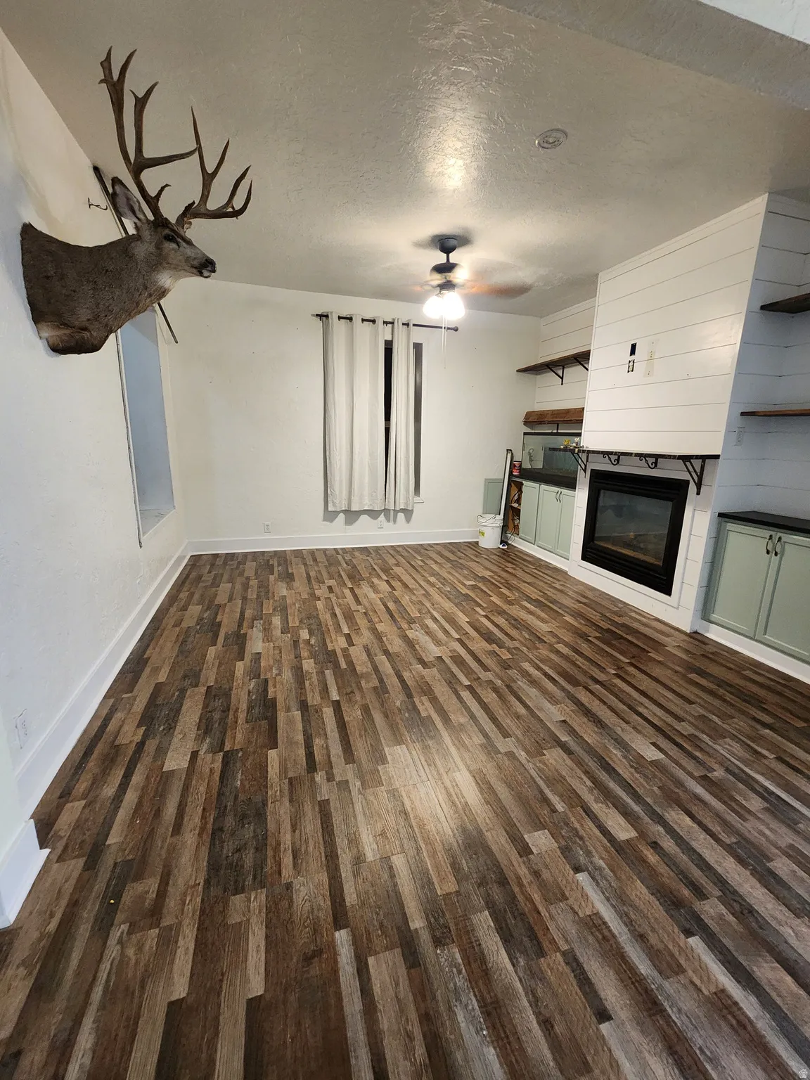 Unfurnished living room featuring a textured ceiling, dark wood finished floors, a fireplace, and a ceiling fan