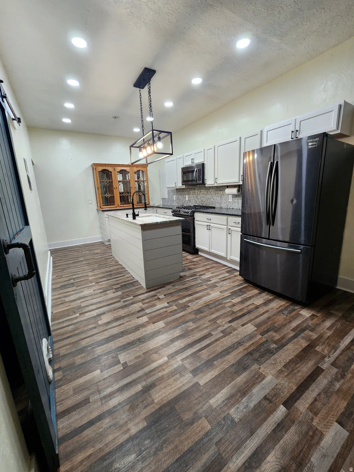 Dual tone kitchen with freestanding refrigerator, range with two ovens, decorative light fixtures, tasteful backsplash, and dark wood finished floors