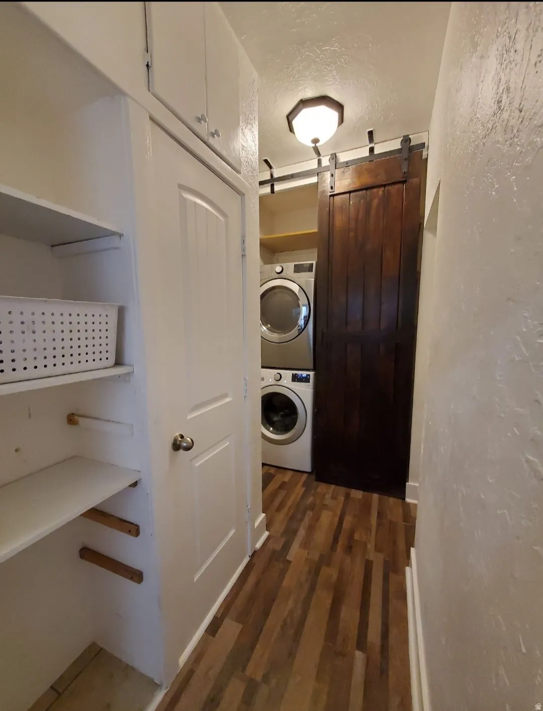 Laundry area featuring a barn door, a textured ceiling, dark wood-style floors, stacked washer and clothes dryer, and a textured wall