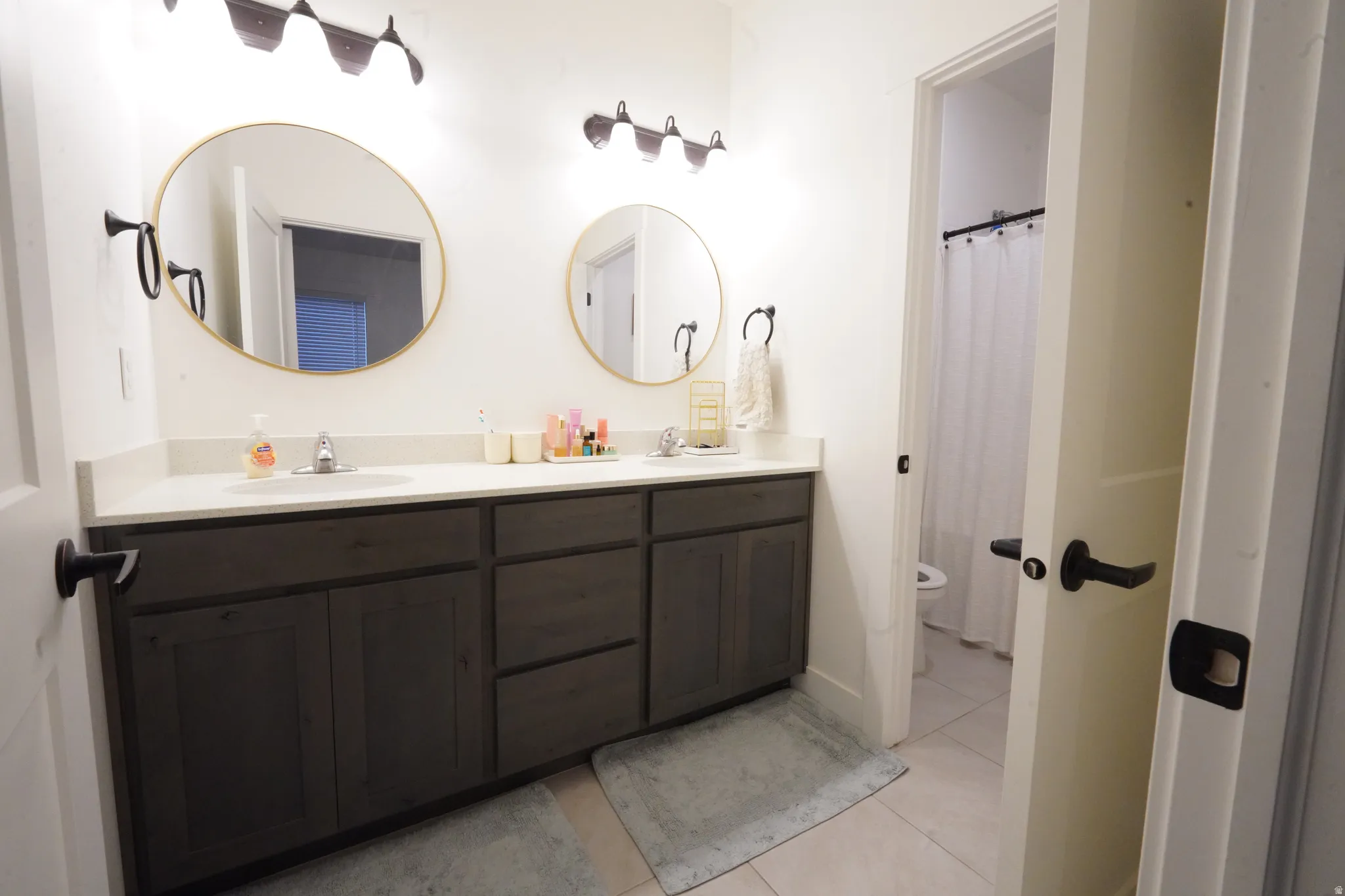 Full bath featuring double vanity, a shower with shower curtain, and light tile patterned floors
