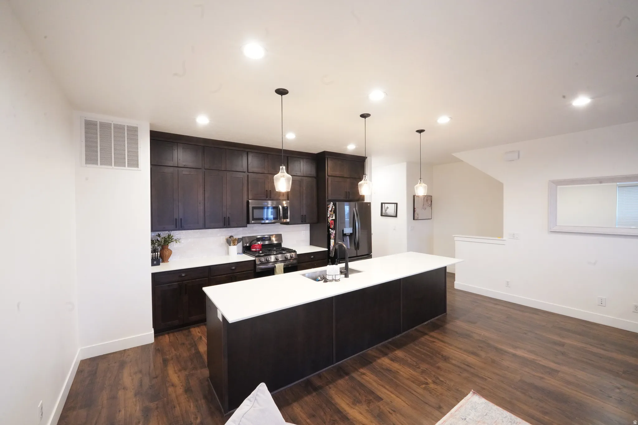 Kitchen with dark wood finish cabinets, stainless steel appliances, a center island with sink, dark wood-type flooring, and decorative light fixtures