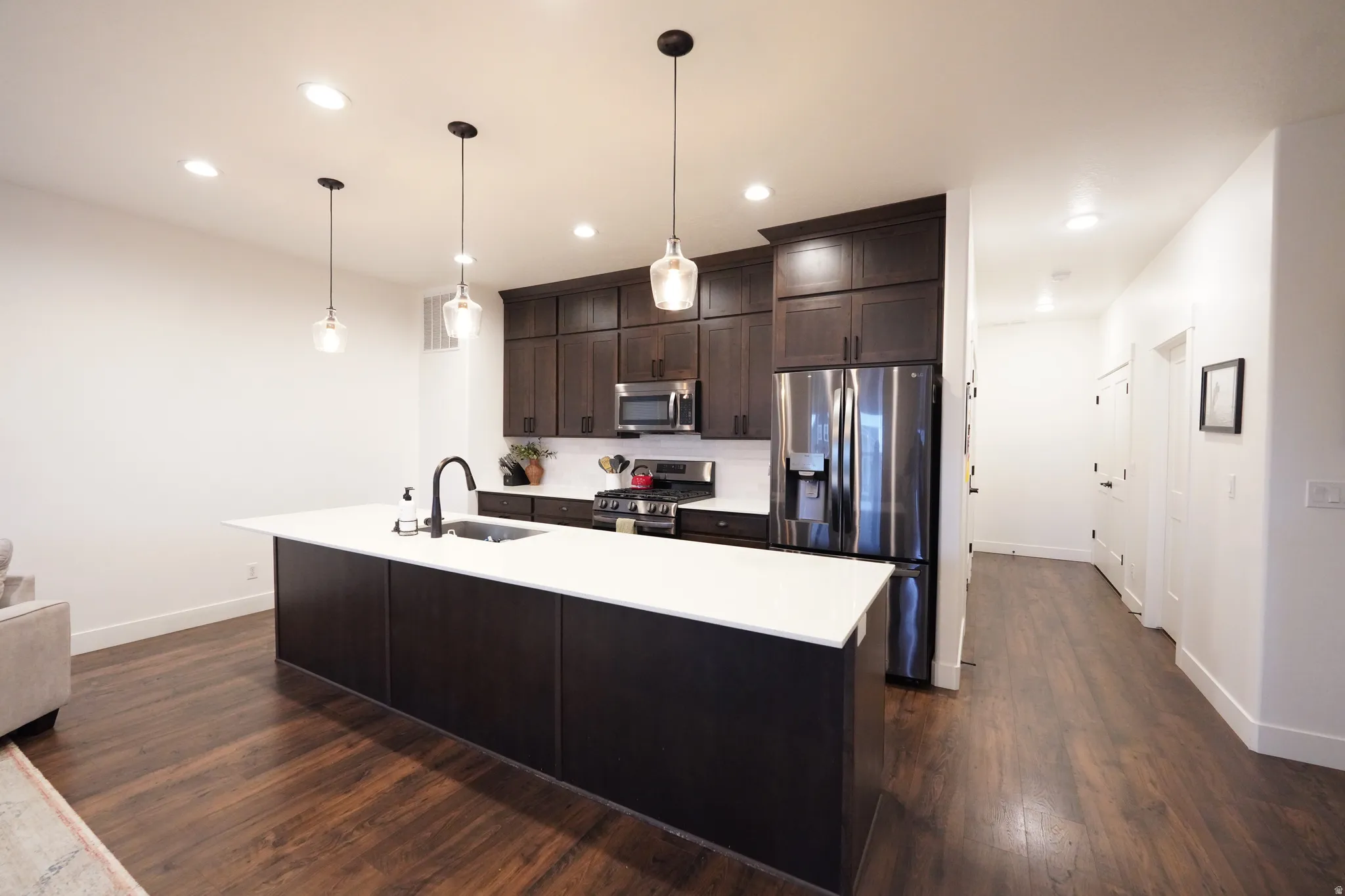 Kitchen with stainless steel appliances, a center island with sink, dark wood finish cabinets, dark wood finished floors, and pendant lighting