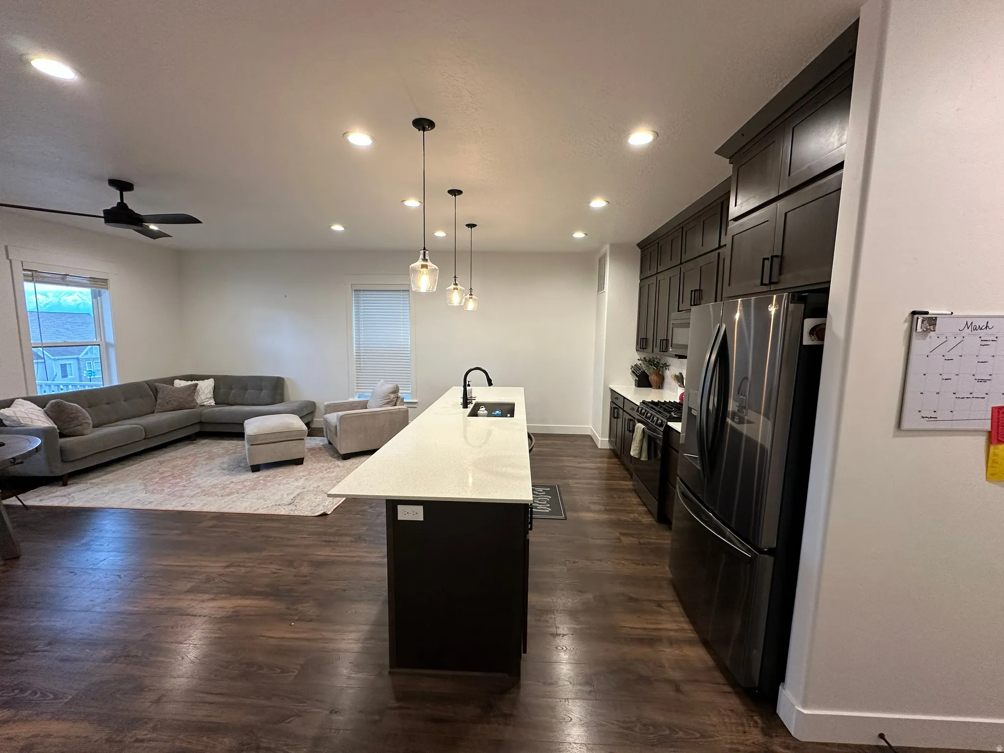 Kitchen with open floor plan, refrigerator with ice dispenser, a kitchen island with sink, pendant lighting, and light stone counters