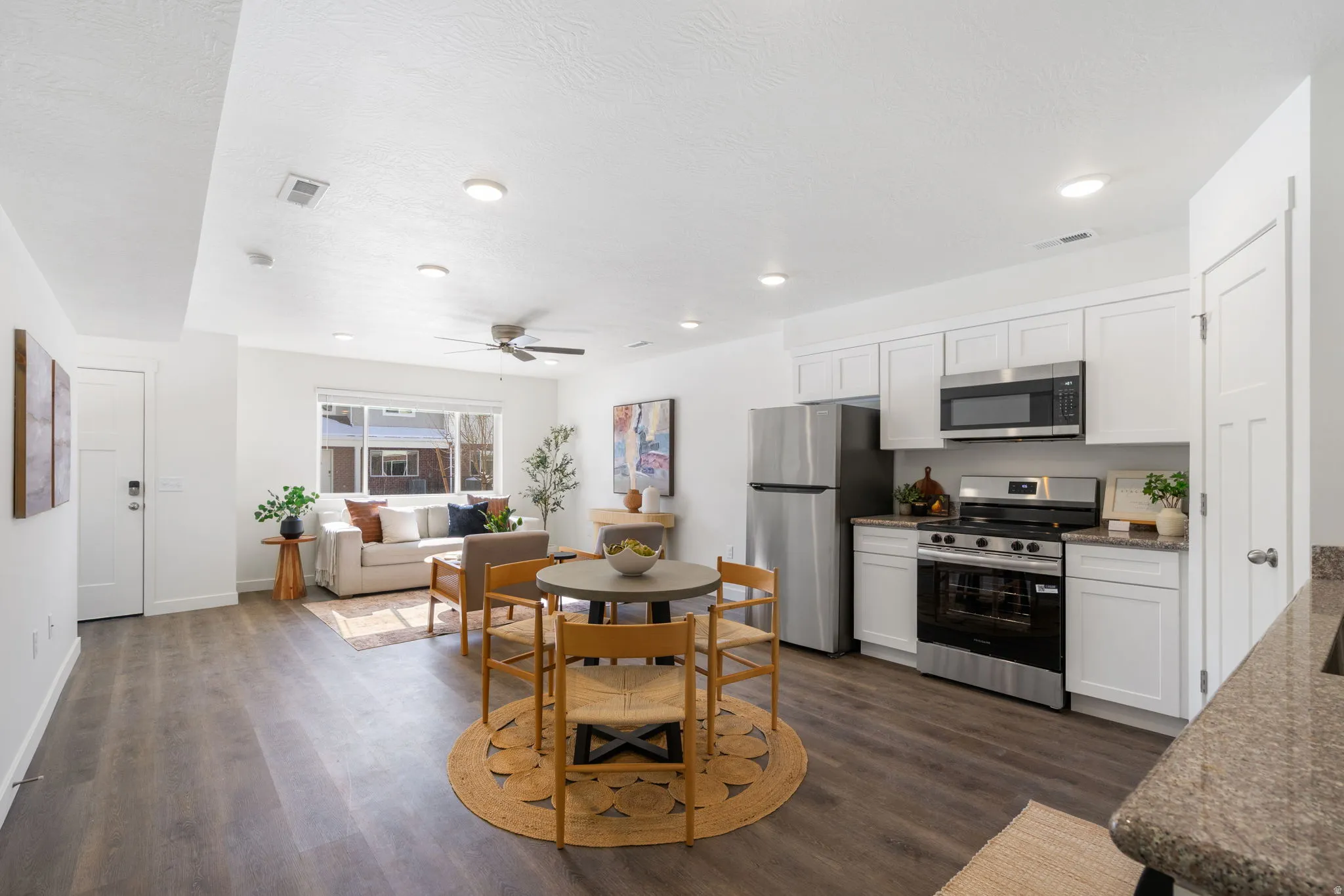 Kitchen with stainless steel appliances, white cabinetry, dark wood-type flooring, and dark stone counters