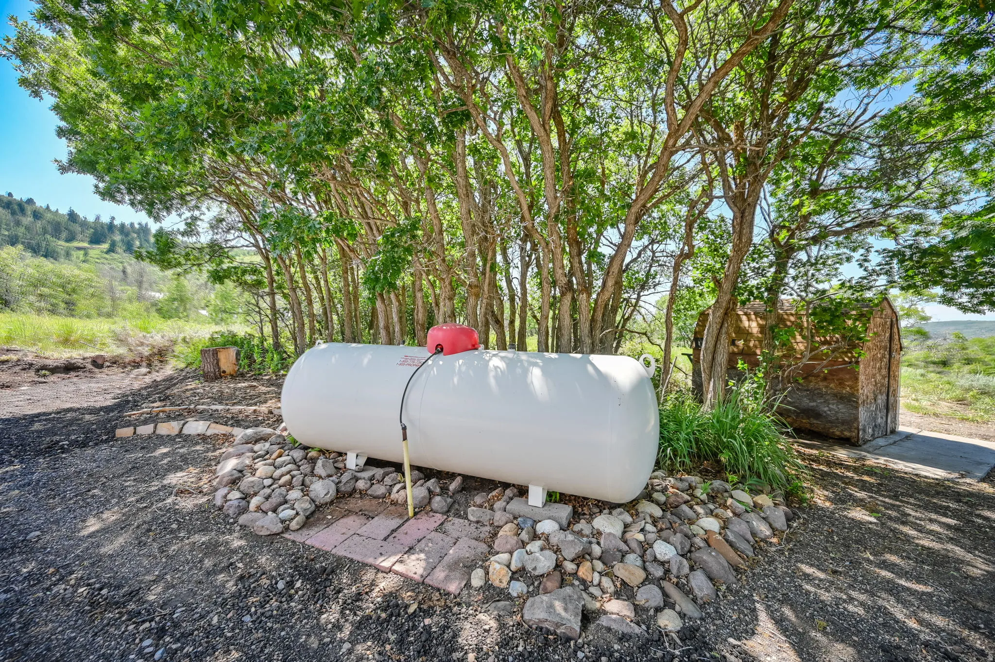 Propane tank installation with a surrounding rock bed and brick pavers