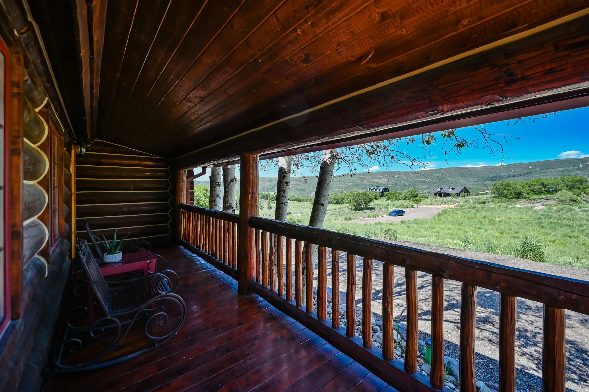 Expansive covered porch featuring wood-finish flooring, log walls, and a rustic wood railing