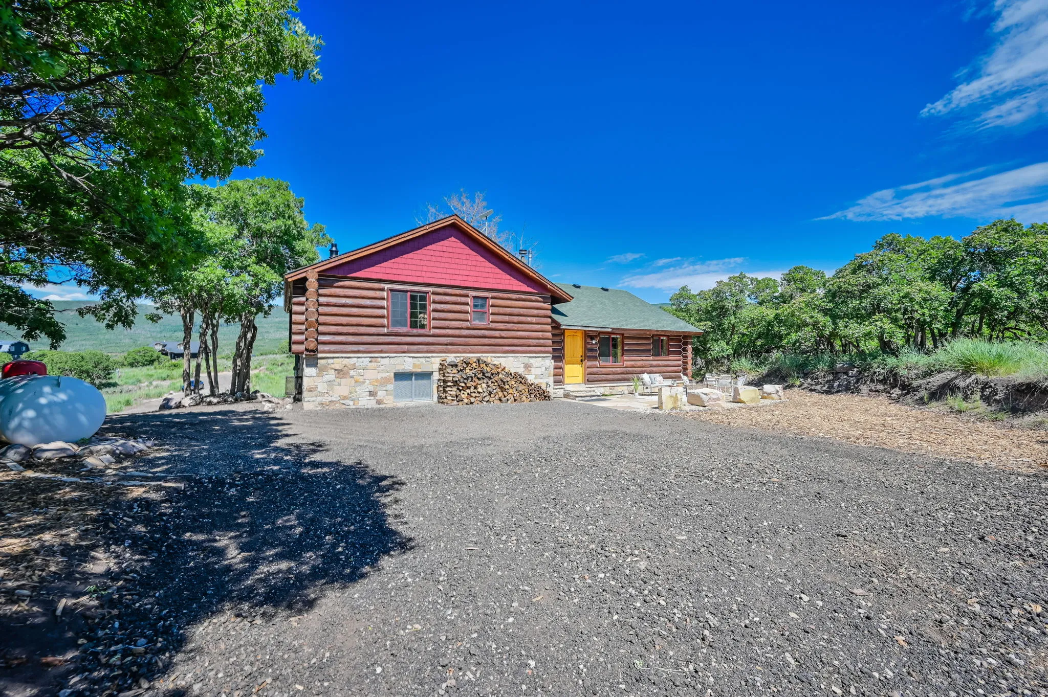 Log cabin exterior with stone foundation, red gables, and a prominent yellow entry door