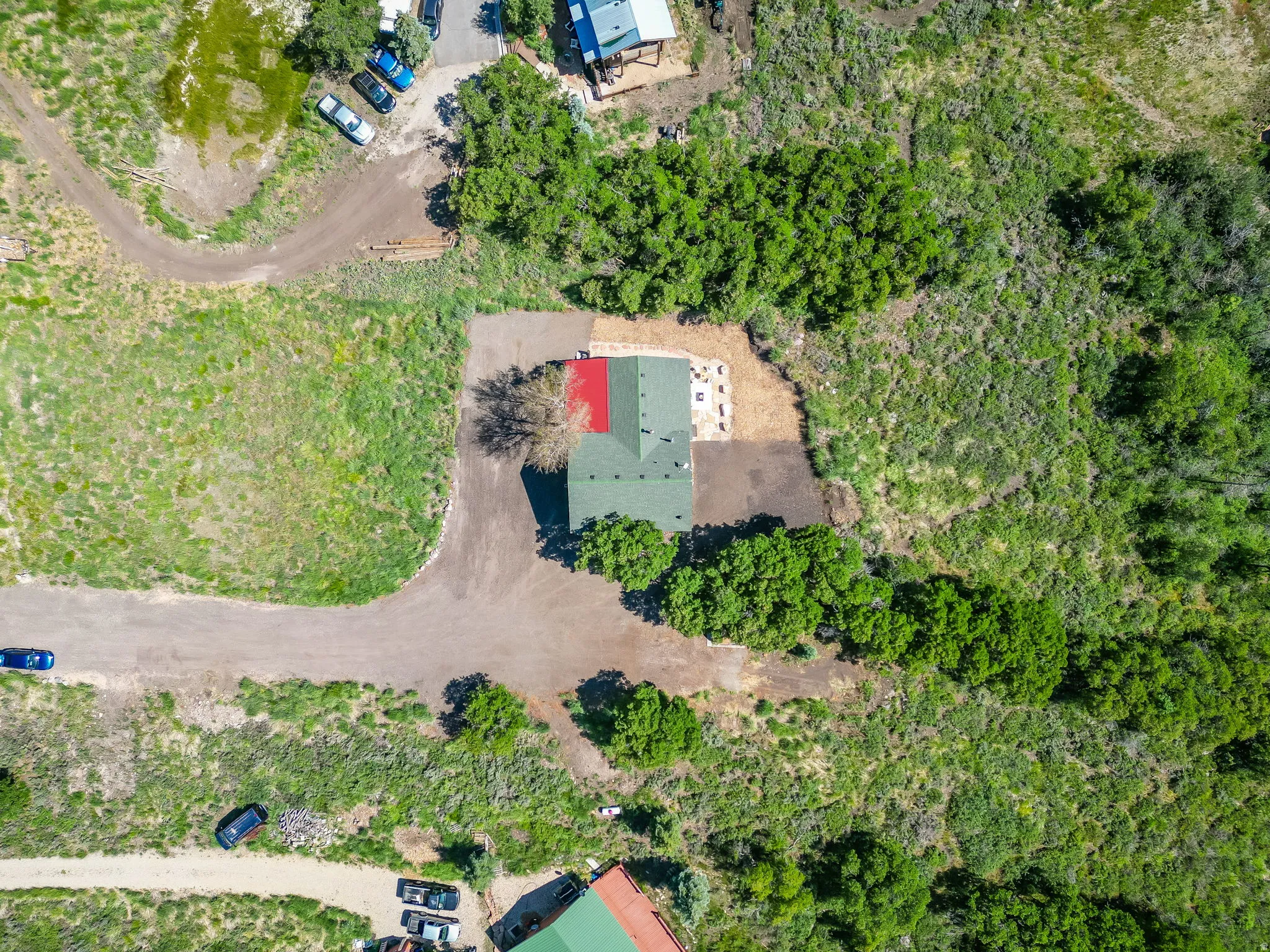 Aerial view of a property featuring a green-roofed structure with a red section, surrounded by natural landscaping and mature trees