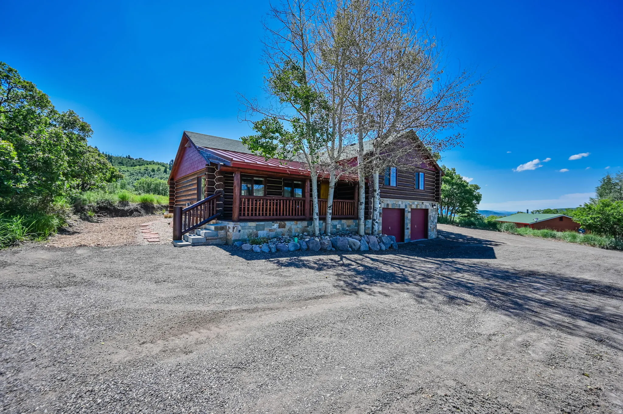Log home featuring a red metal roof, stone foundation, and a covered front porch with wood railings