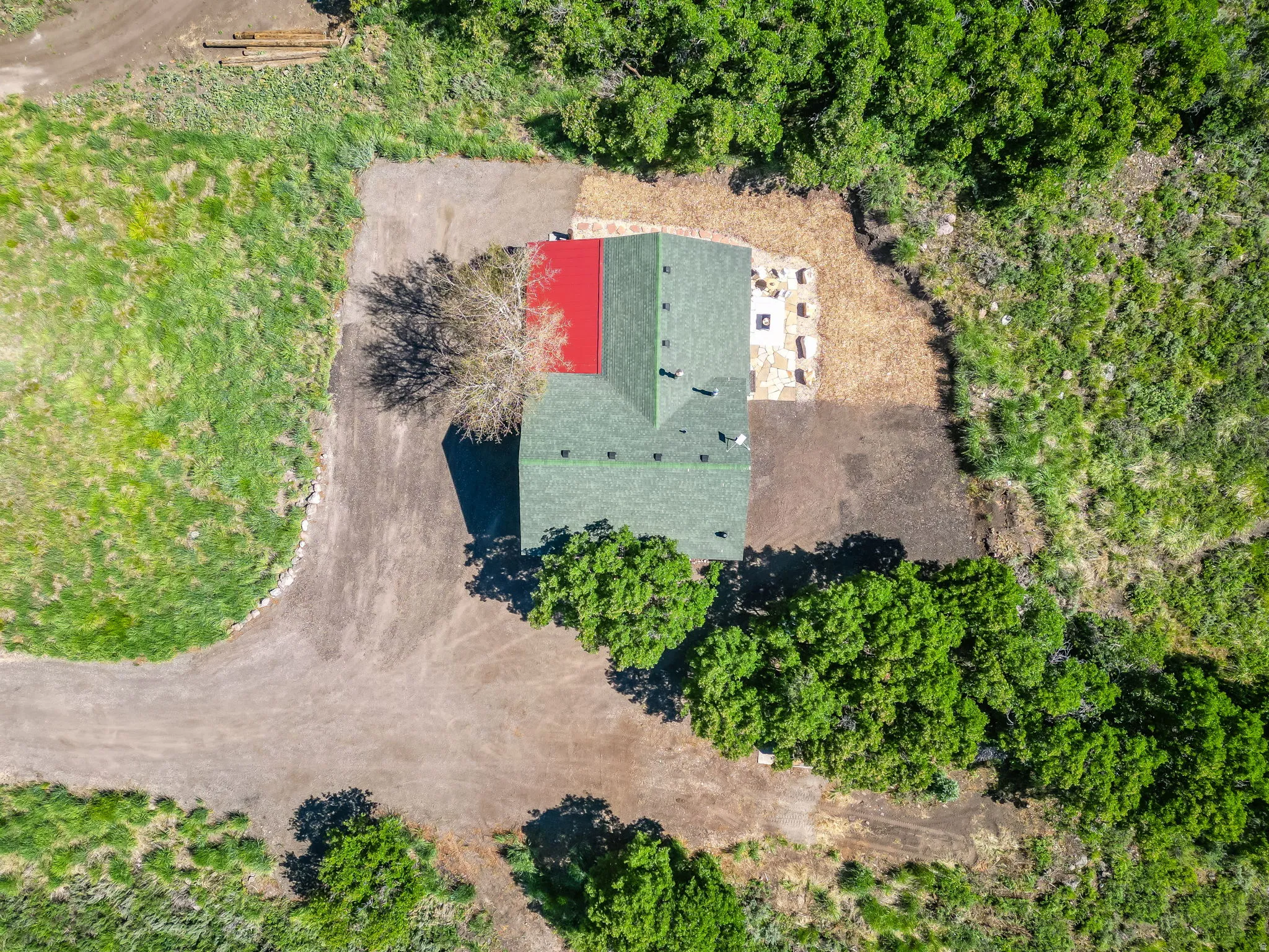 Overhead property view featuring a green asphalt shingle roof with a red section, surrounded by natural landscaping