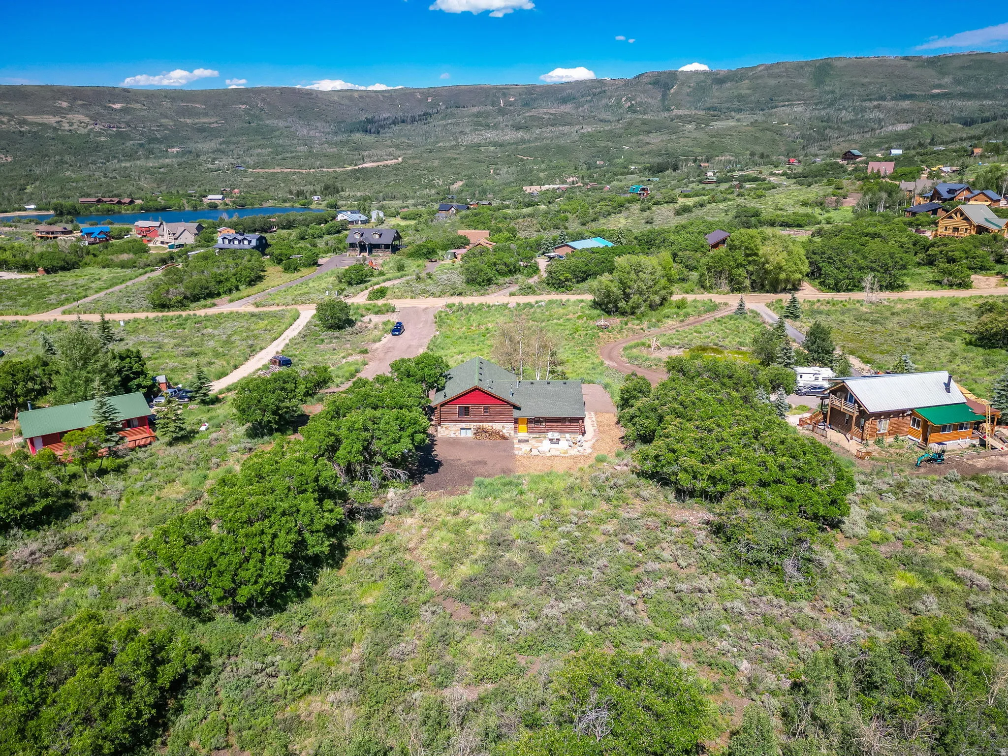 Mountain property featuring a single-story residence with a red exterior and green roof, surrounded by natural landscaping