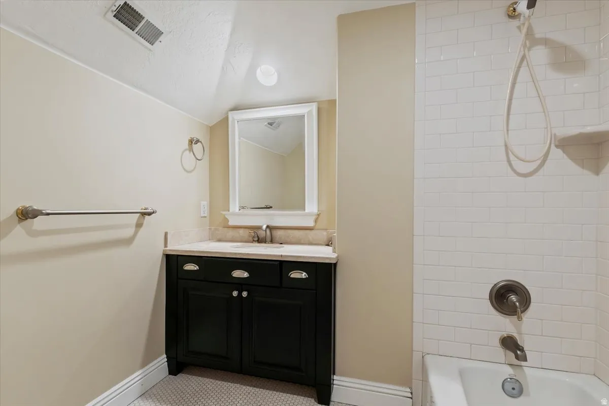 Bathroom featuring vanity, vaulted ceiling, and washtub / shower combination