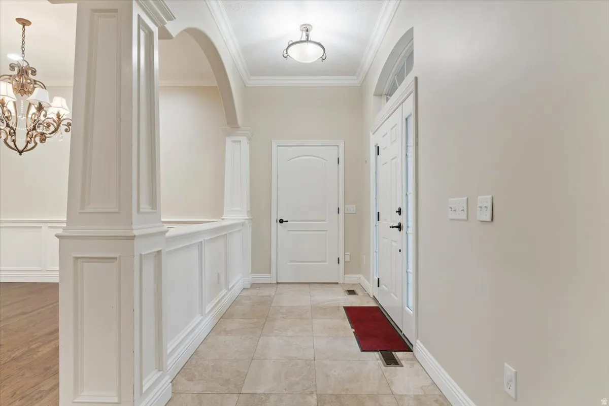 Entryway featuring crown molding, a chandelier, a decorative wall, and arched walkways