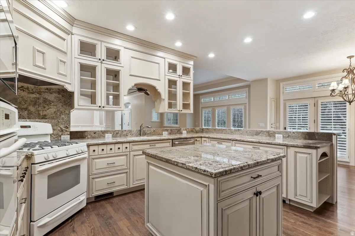 Kitchen with a peninsula, white appliances, a center island, and light stone counters