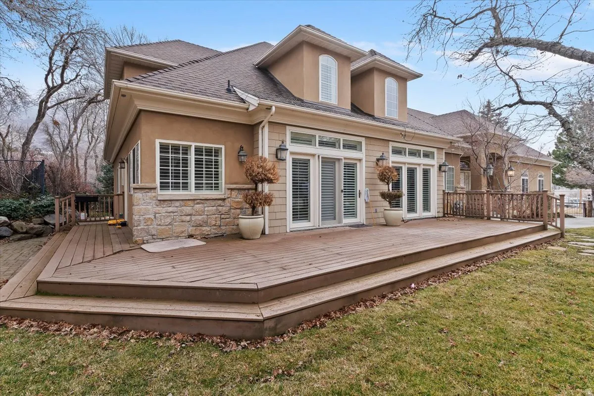 Back of house featuring a deck, stucco siding, roof with shingles, stone siding, and a yard