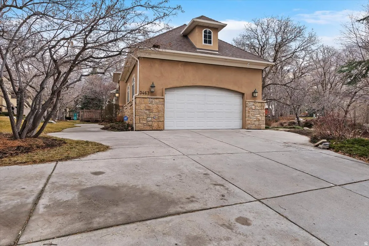 View of property exterior featuring stone siding, stucco siding, concrete driveway, and roof with shingles