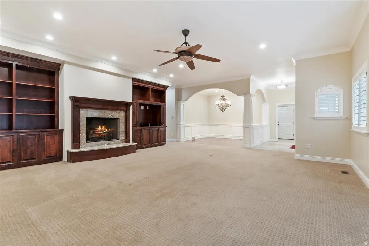 Unfurnished living room featuring ceiling fan, built in features, arched walkways, carpet, and a premium fireplace