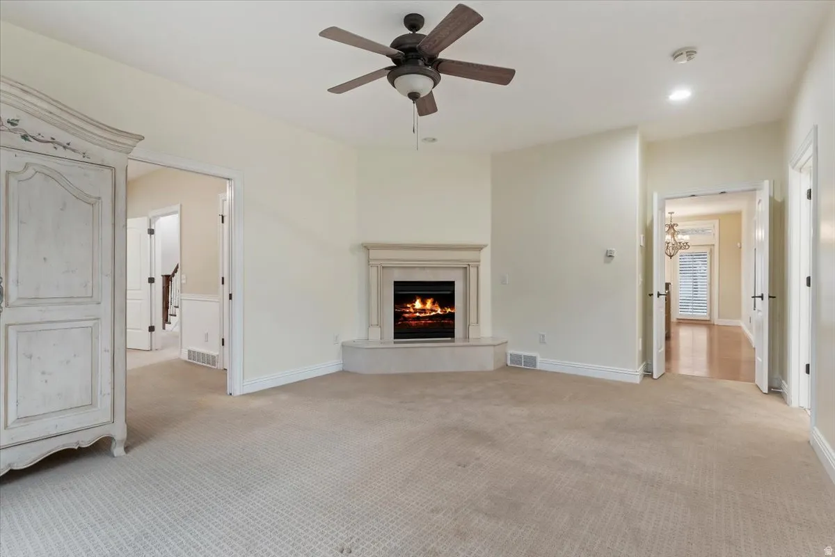Unfurnished living room with a ceiling fan, a premium fireplace, light carpet, and recessed lighting