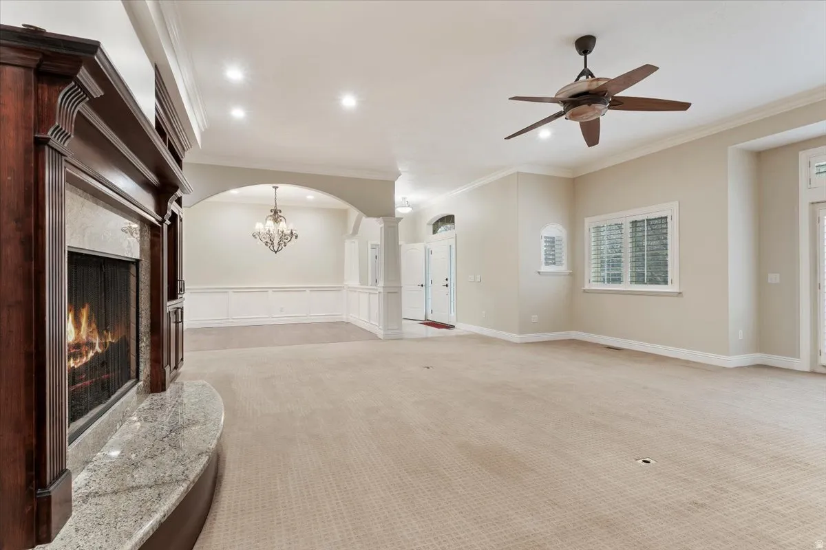 Unfurnished living room with a premium fireplace, light colored carpet, arched walkways, ceiling fan, and ornamental molding