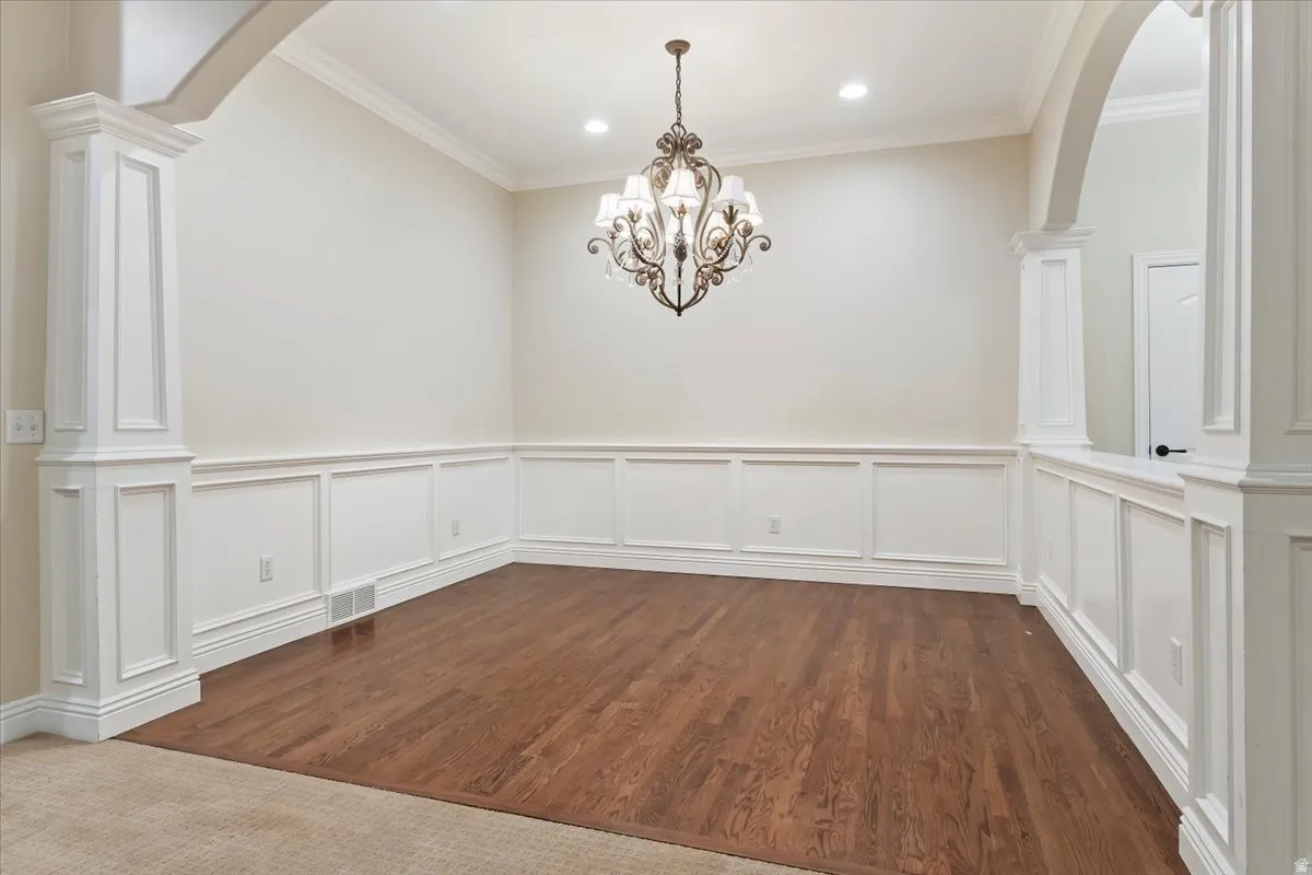 Unfurnished dining area with arched walkways, decorative columns, crown molding, hanging lights, and a wainscoted wall