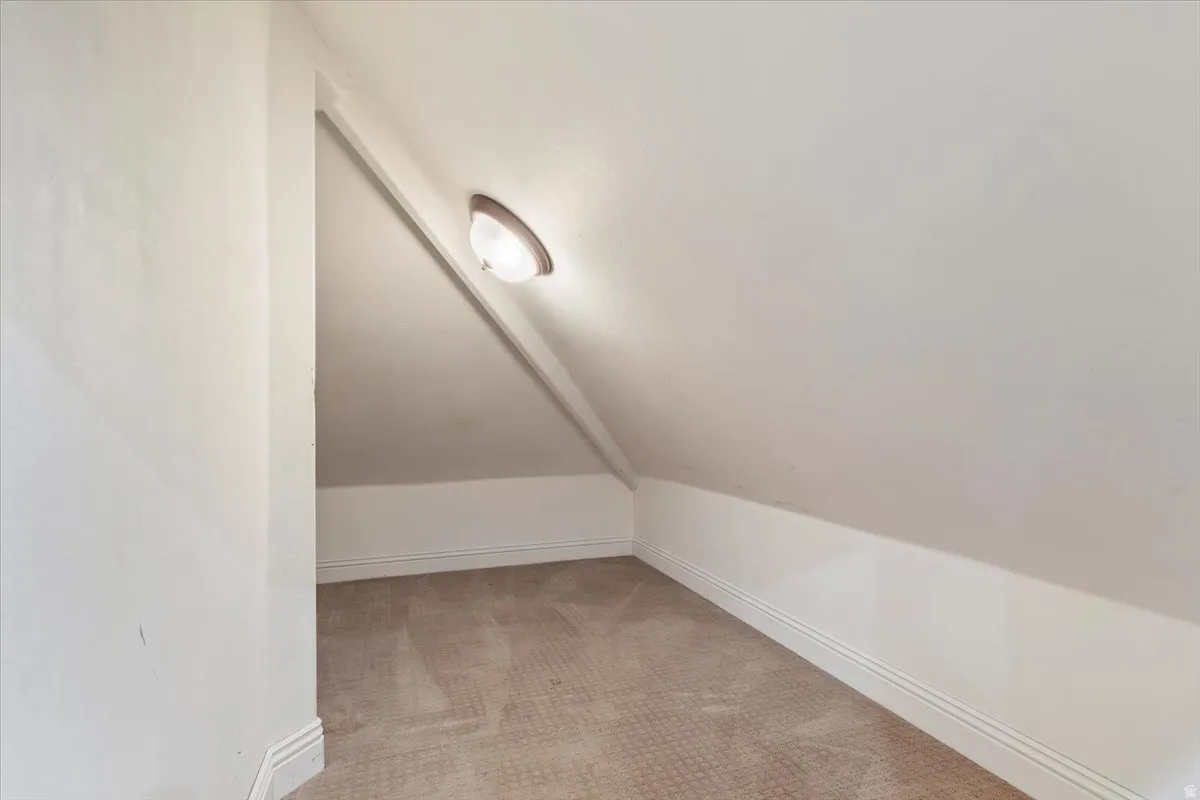 Bonus room with light colored carpet and vaulted ceiling