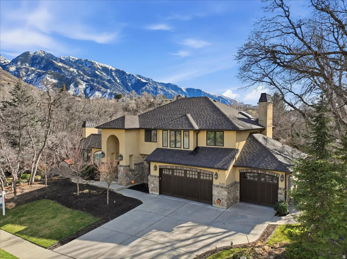 View of front of house featuring a chimney, stucco siding, driveway, a mountain view, and stone siding