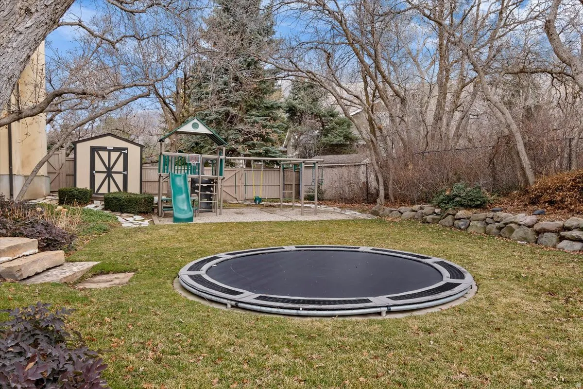 Fenced yard with a playground, a storage shed, a trampoline, and a patio
