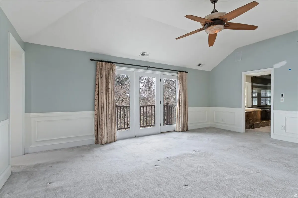 Carpeted empty room with wainscoting, a decorative wall, ceiling fan, and vaulted ceiling
