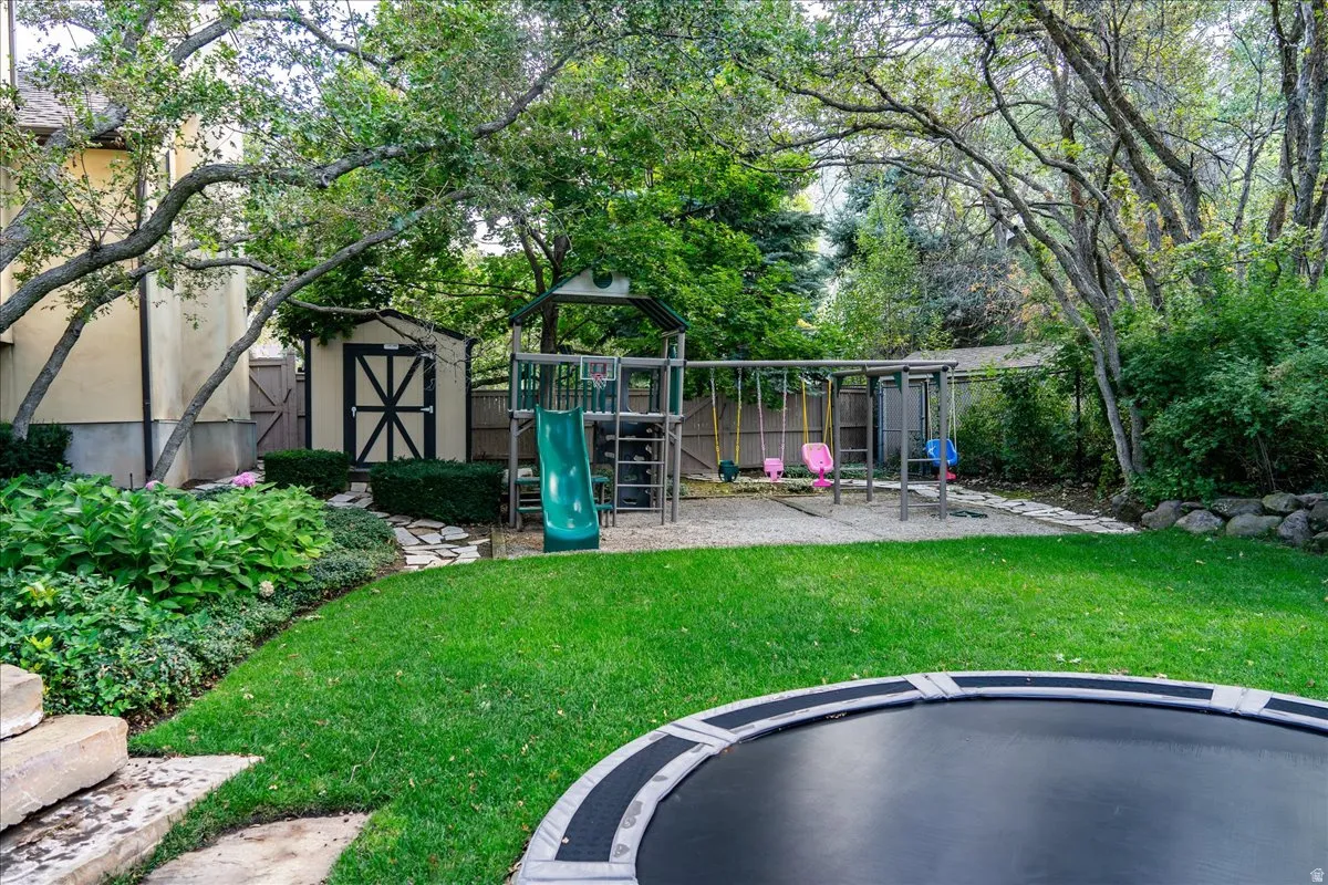 Fenced yard featuring a playground, a trampoline, a storage shed, and a patio