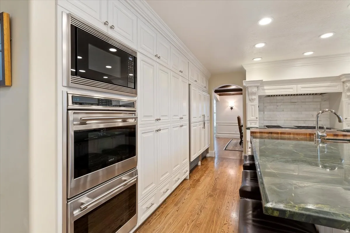Kitchen with stainless steel double oven, arched walkways, built in microwave, recessed lighting, and white cabinetry