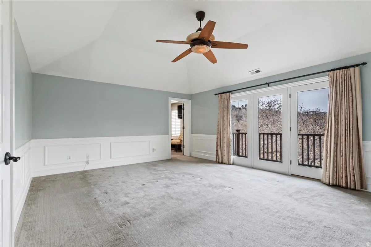 Unfurnished bedroom featuring a wainscoted wall, carpet floors, a decorative wall, access to outside, and a ceiling fan