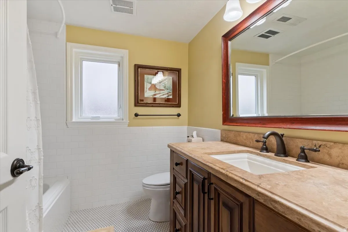 Full bath with vanity, tile walls, a wainscoted wall, shower / bath combo with shower curtain, and tile patterned floors