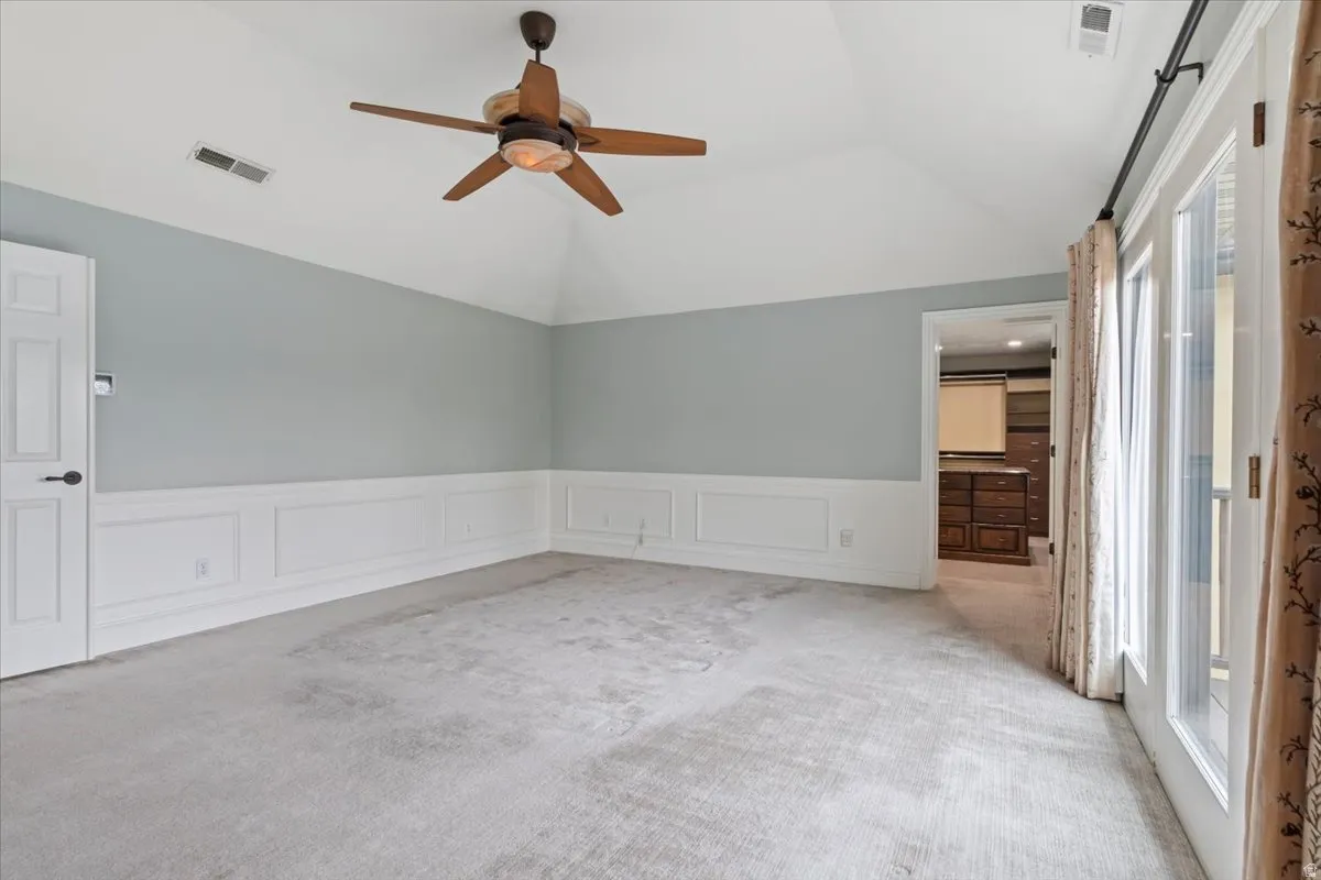 Unfurnished room with light carpet, a decorative wall, a wainscoted wall, ceiling fan, and lofted ceiling