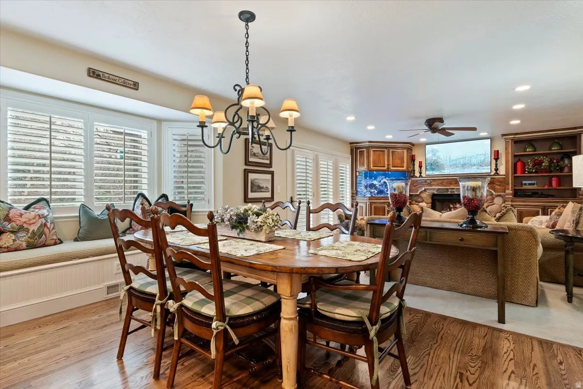 Dining space with hanging lights, a stone fireplace, light wood-style flooring, and a ceiling fan