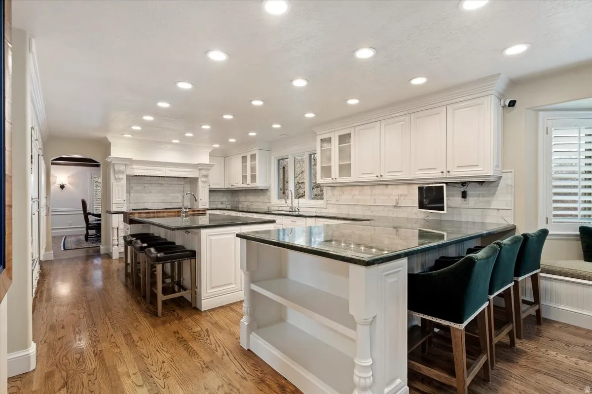 Kitchen featuring a kitchen breakfast bar, a peninsula, white cabinets, a center island with sink, and glass fronted cabinets