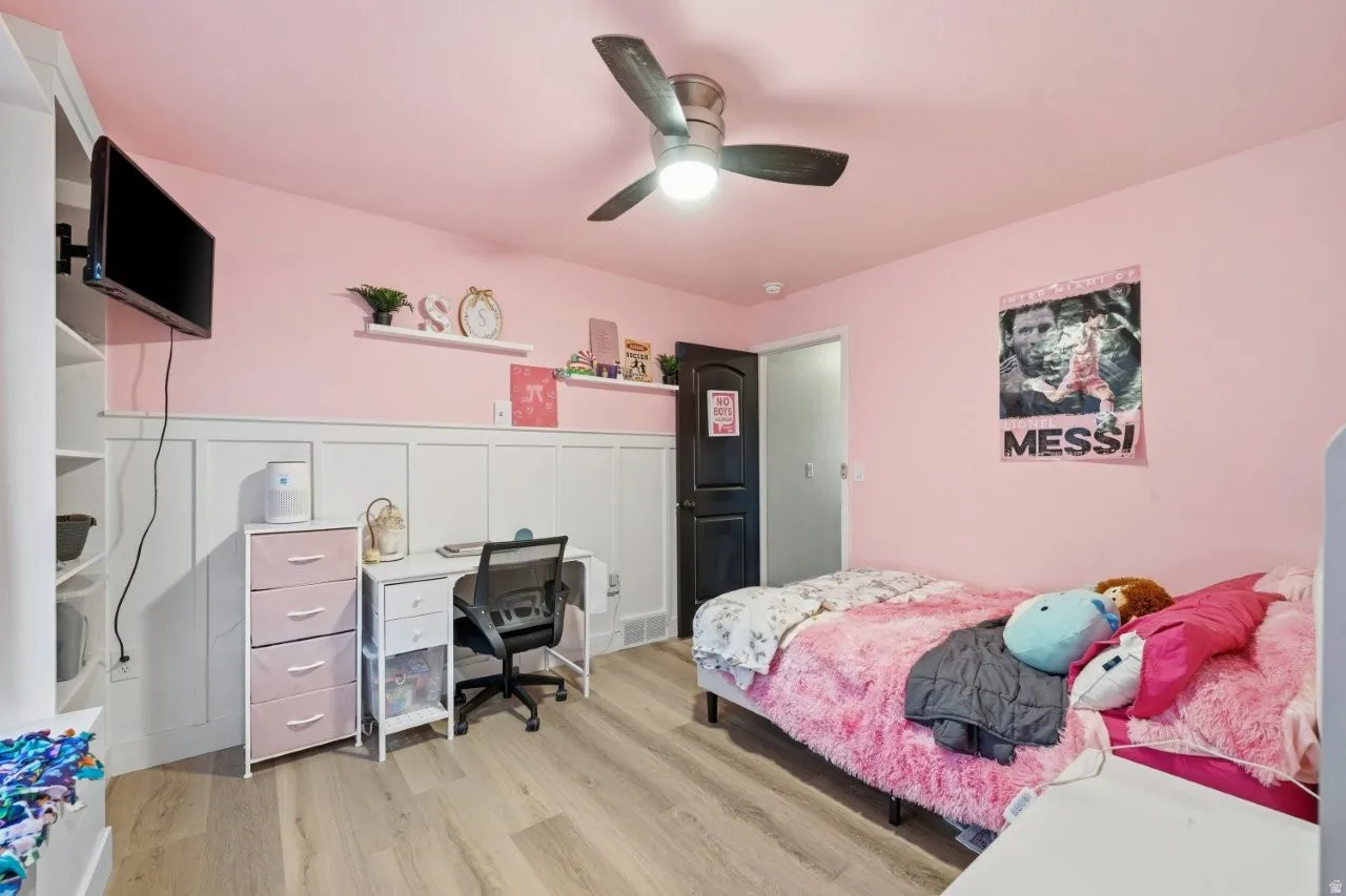 Bedroom featuring an office area, light wood finished floors, a ceiling fan, and wainscoting