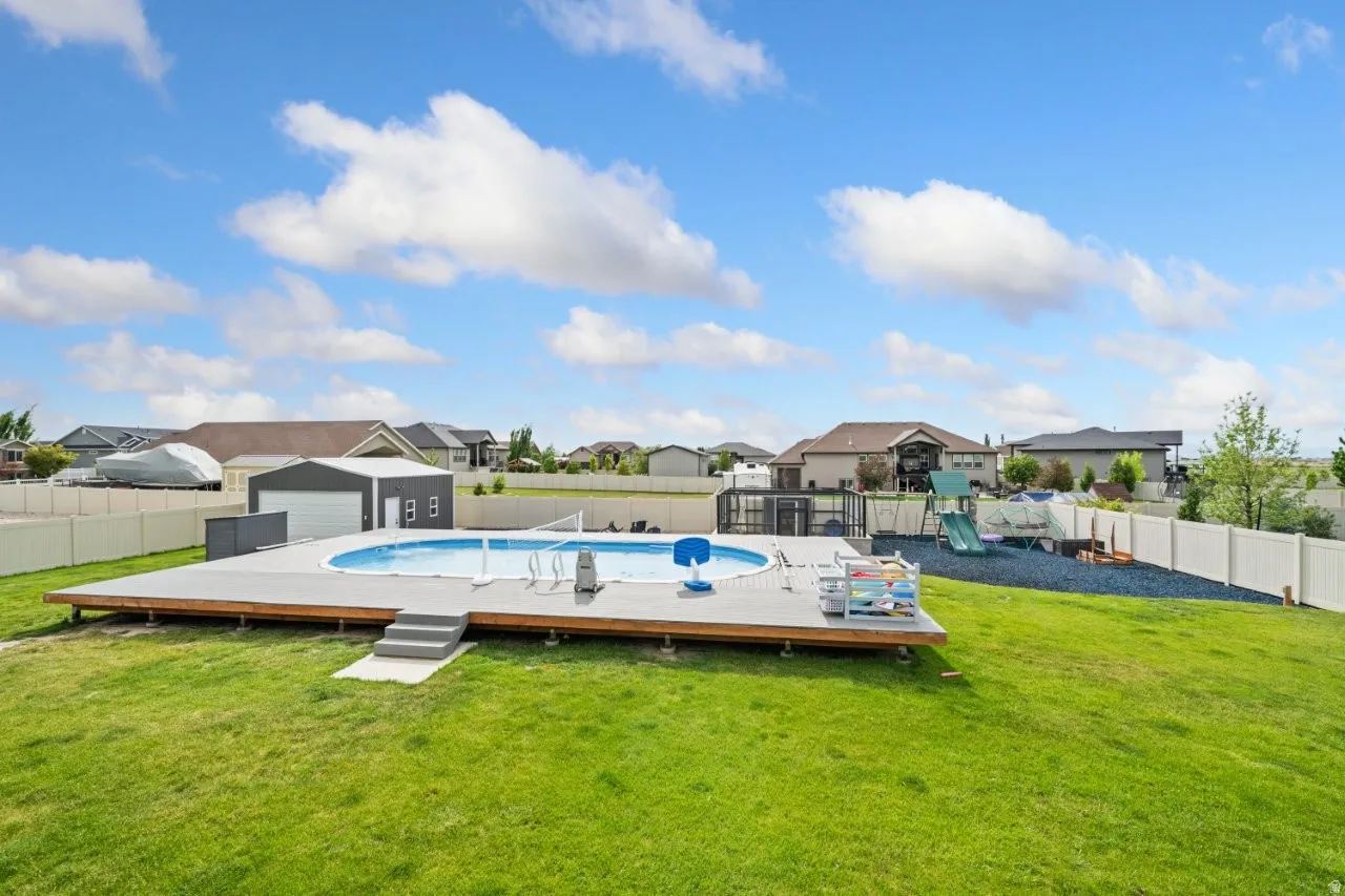 Expansive backyard featuring a large above-ground swimming pool with a surrounding wood-finish deck, a detached metal garage, and a white privacy fence