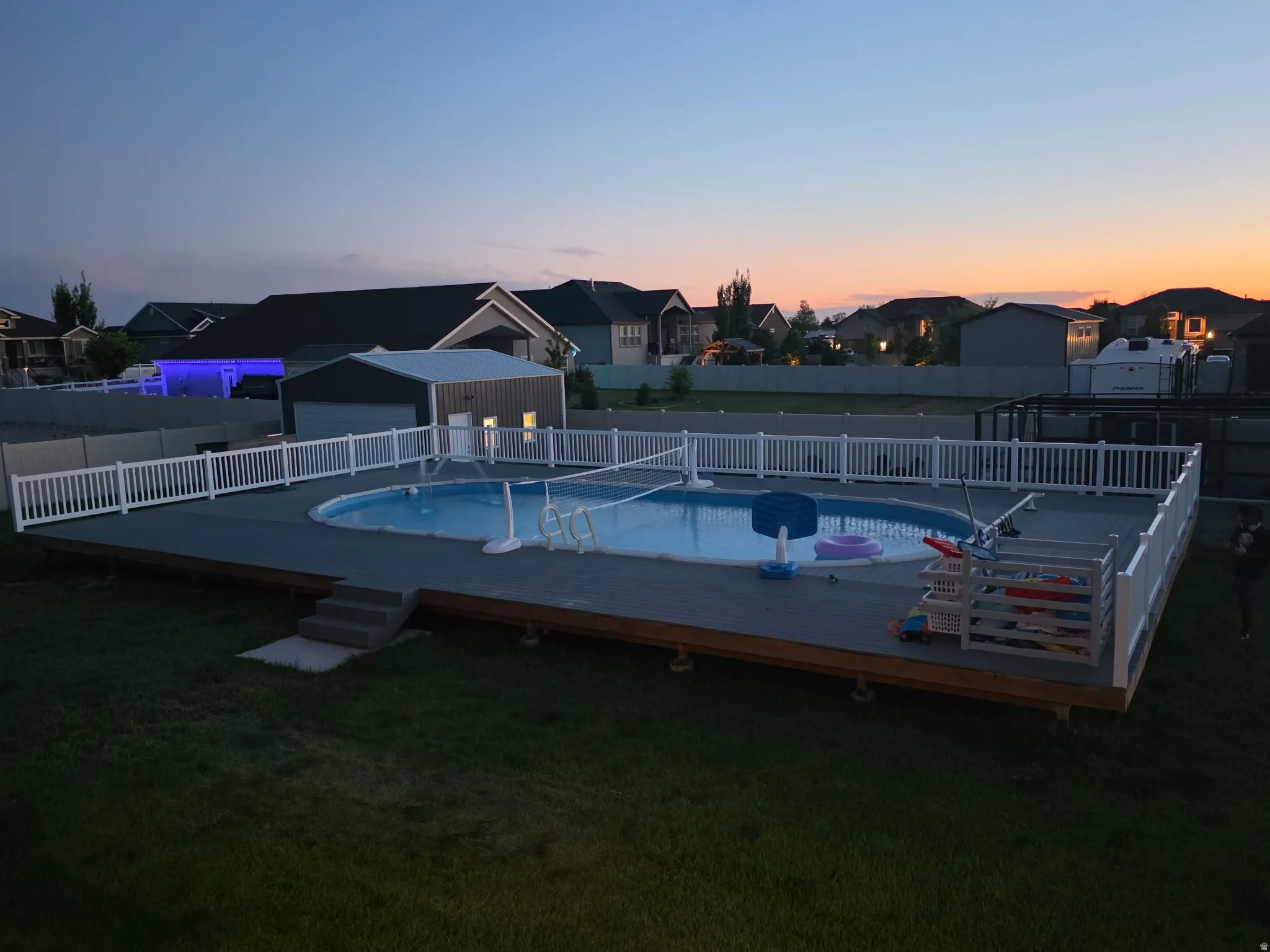 Oval-shaped swimming pool surrounded by a composite deck with white fencing