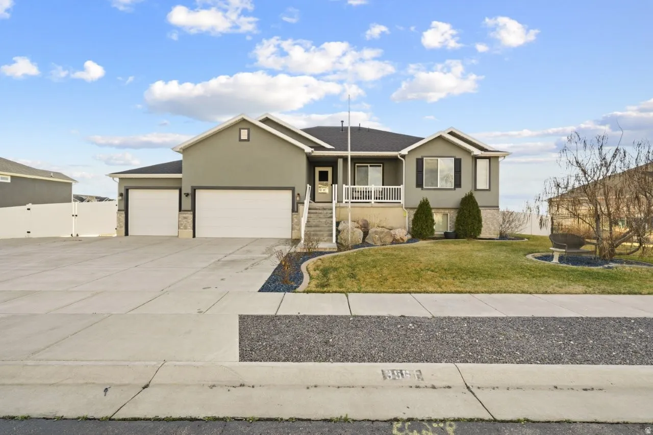 Ranch-style house with a garage, stucco siding, driveway, a gate, and a front lawn