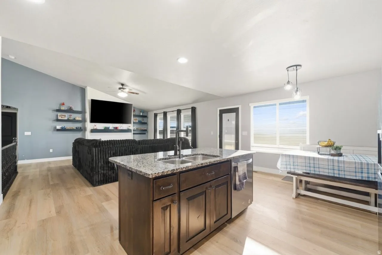 Kitchen featuring open floor plan, dark wood finish cabinets, vaulted ceiling, pendant lighting, and a center island with sink