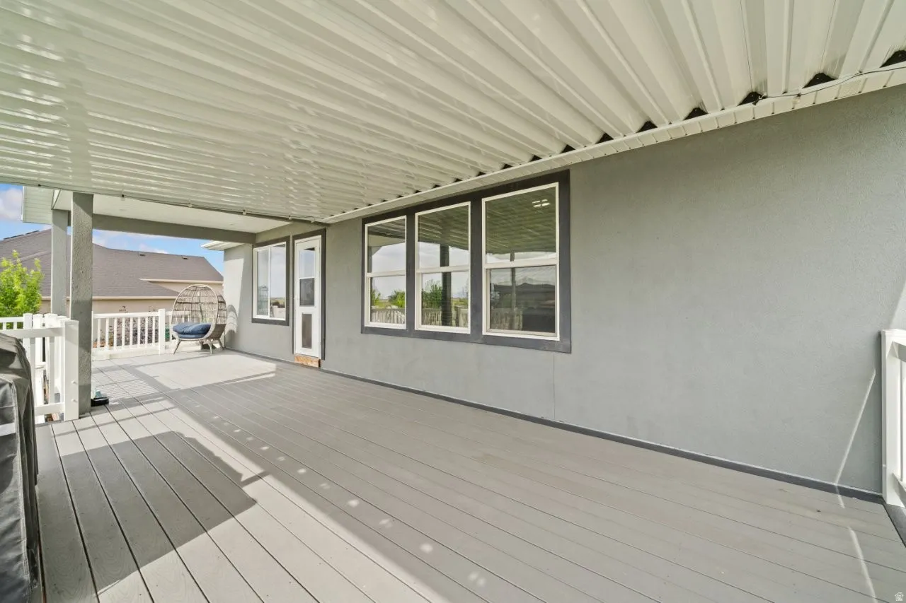 Expansive covered patio featuring composite decking, a white railing, and a textured grey exterior wall with multiple windows