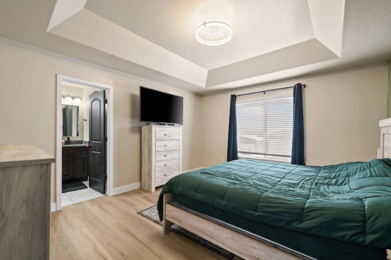 Spacious room featuring tray ceilings with a flush mount light fixture, wood-finish flooring, and a large window