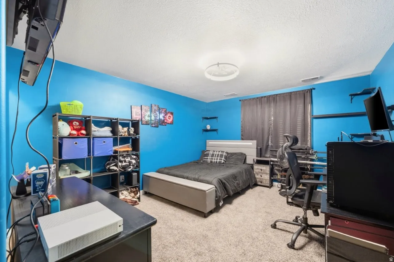 Bedroom with an office area, light colored carpet, and a textured ceiling