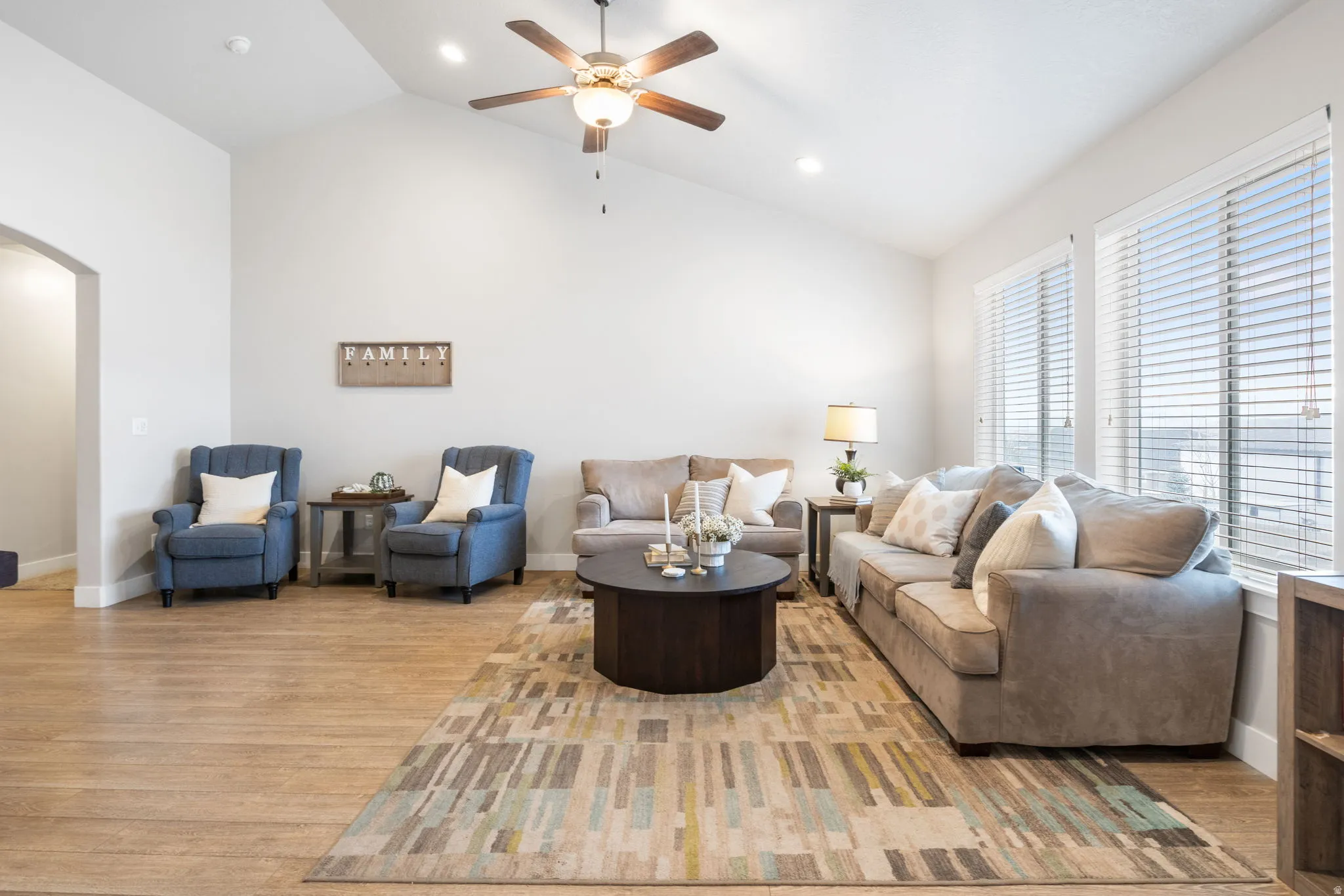 Living area with arched walkways, a ceiling fan, lofted ceiling, light wood-style flooring, and recessed lighting