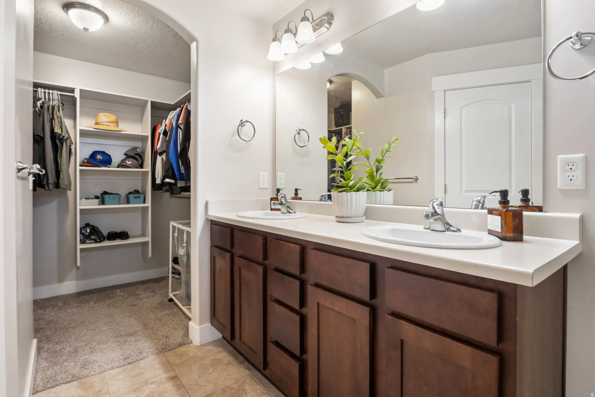 Bathroom featuring double vanity, a spacious closet, light colored carpet, and a textured ceiling