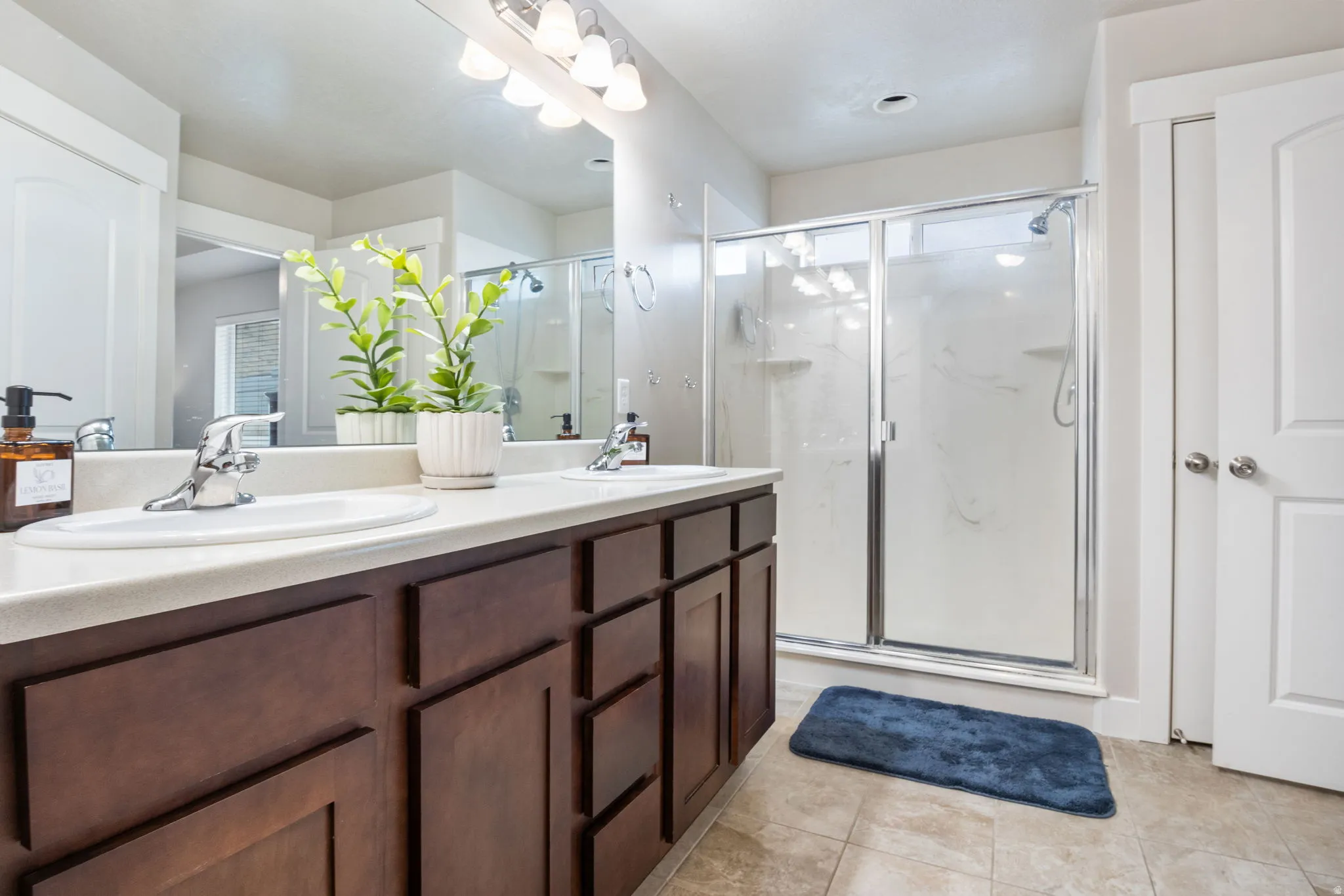 Bathroom with double vanity, a marble finish shower, and light tile patterned floors